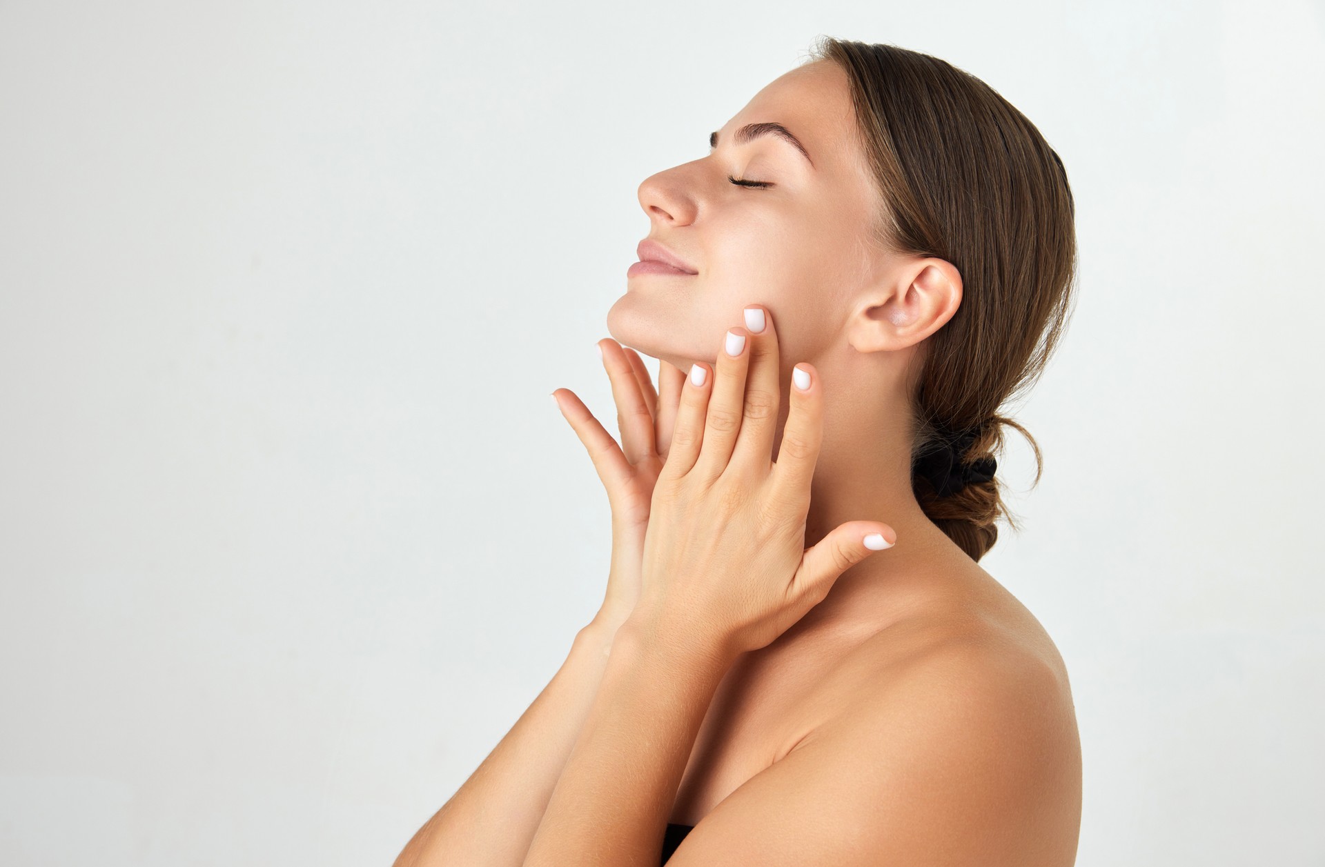 Side view. Young woman taking care after skin, doing face massage with hands isolated on white background. Lifting