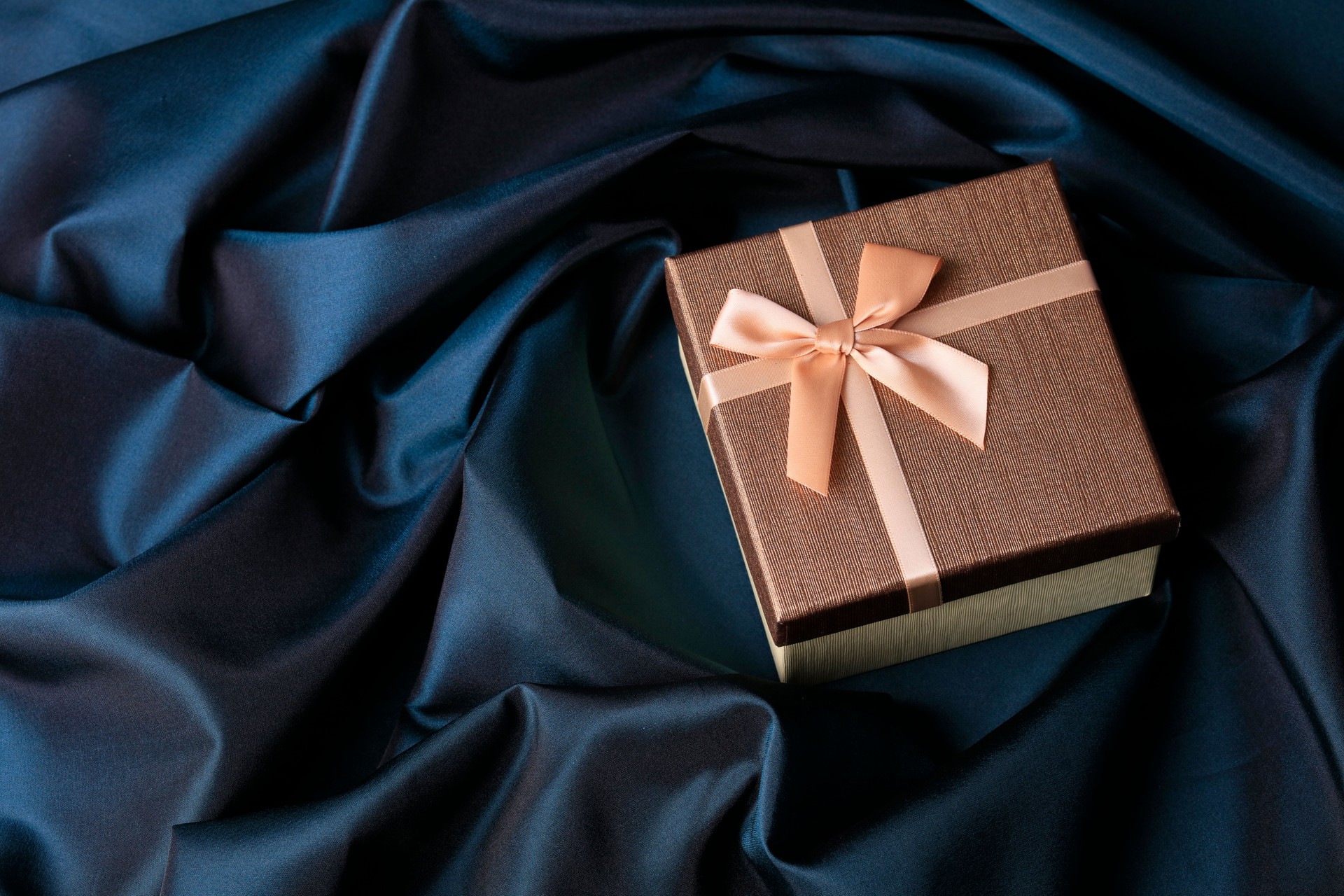 Golden gift box on navy blue satin background Golden gift box on navy blue satin background